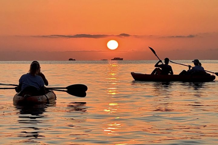 Two kayaks on calm water at sunset with an orange sky and visible sun.