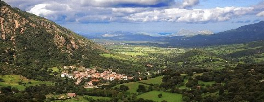 Scenic view of a village nestled in a green valley with mountains and cloudy sky.