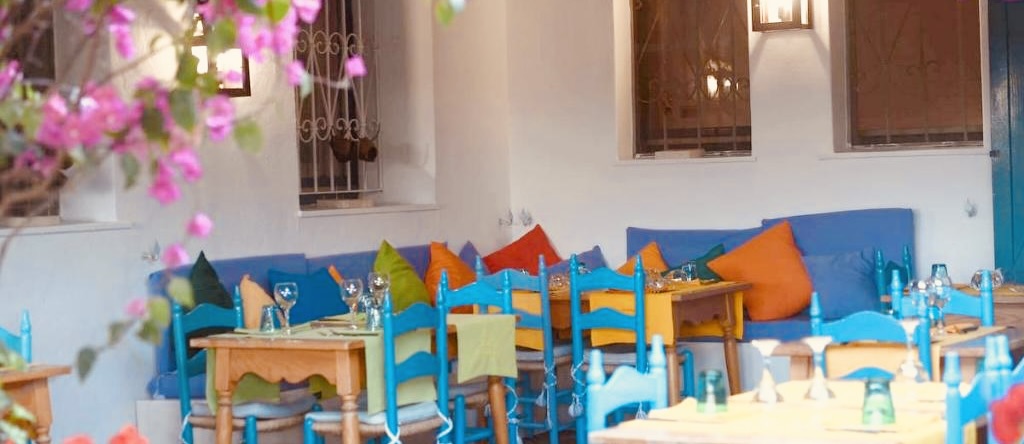 Outdoor cafe with blue chairs, colorful cushions, and pink flowers.