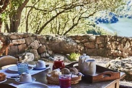 Outdoor table with breakfast set, stone wall, trees, and a river view in the background.