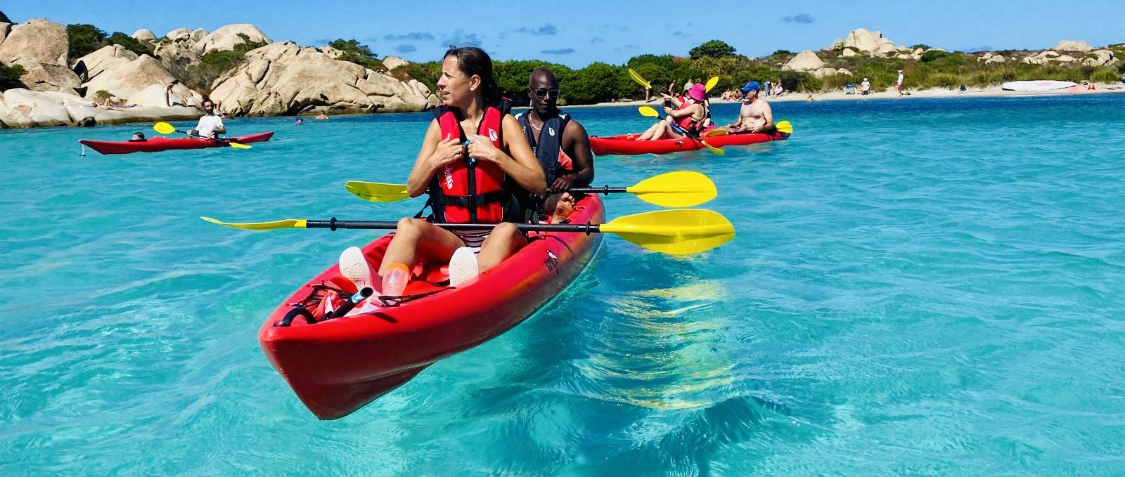 People kayaking on clear blue water near rocky shores under a sunny sky.