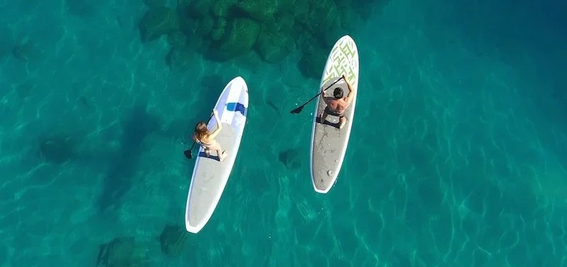 couple-doing-standup-paddle-at-lake-tahoe a person riding a surf board on a body of water