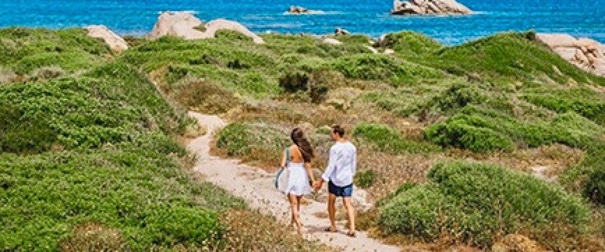 Couple walking on a grassy path near the ocean.