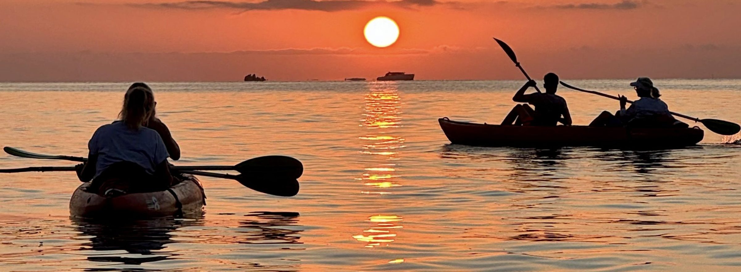 Two kayaks on calm water at sunset with orange sky and sun reflection.