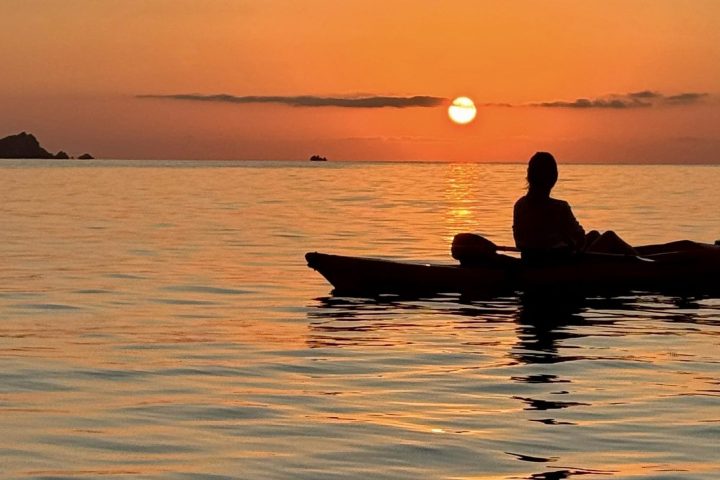 Silhouette of a person on a kayak during a sunset over calm water.