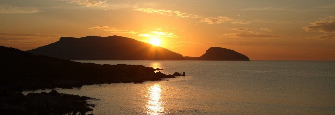 Sunset over ocean with dark silhouetted hills and calm water.