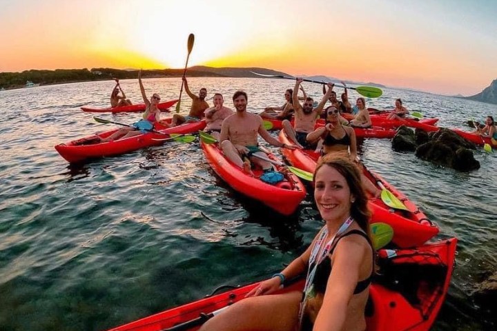 Group of people kayaking on a lake during sunset, smiling and posing for a photo.