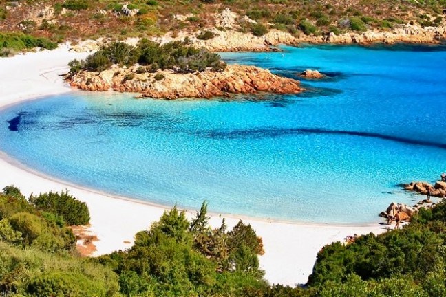 Scenic beach with white sand, clear turquoise water, and rocky shoreline.
