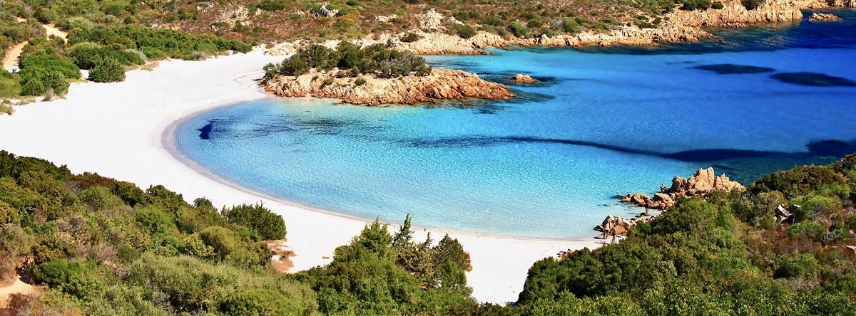 Scenic beach with white sand, clear turquoise water, and rocky shoreline.